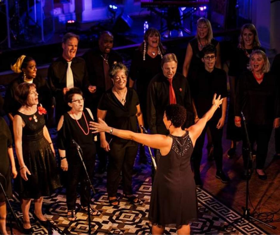 A picture of Bright Soul Choir performing at a concert. Choir members are dressed in smart black clothing with splashes of colour.